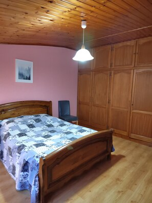 Een slaapkamer met een houten bed, een stoel, een kledingkast en een plafondlamp.