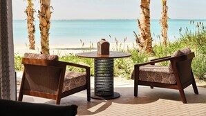 Un espace aménagé avec des sièges au bord de la plage, comprenant deux fauteuils en osier et une table ronde, offrant une vue sur la mer.