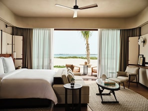 A hotel room with a bed, a sofa, a coffee table, a chair, and a view of the beach.