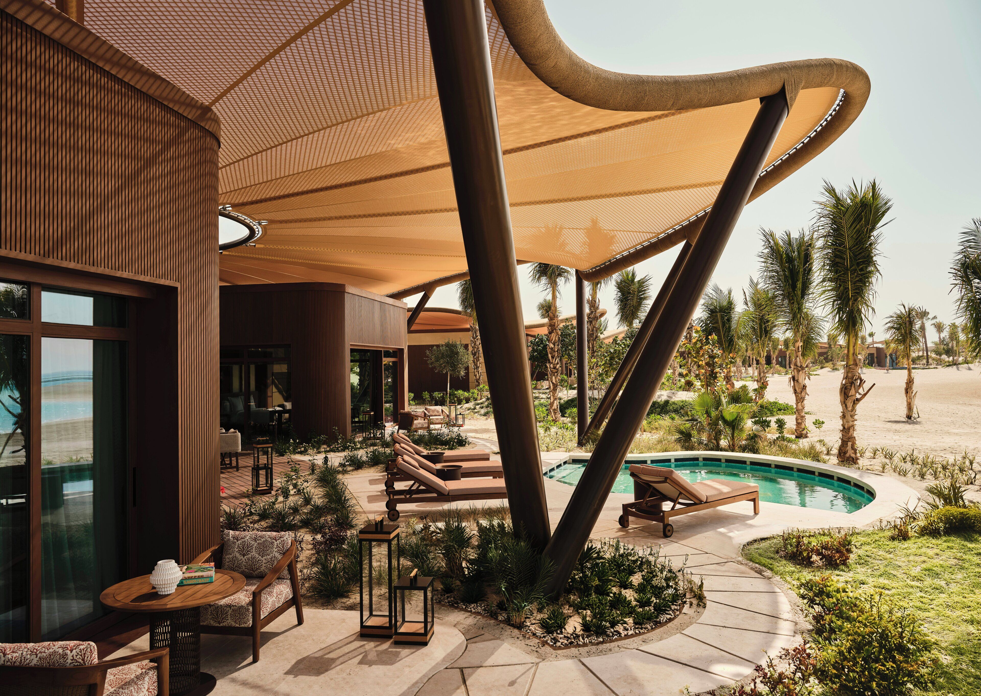 A modern outdoor lounge area with a pool, seating, and a view of the beach.