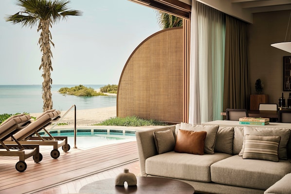 A modern living area with a view of the sea, a pool, and a beach.