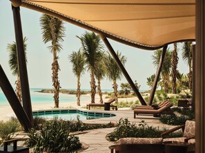 A poolside area with lounge chairs, a pool, and palm trees.
