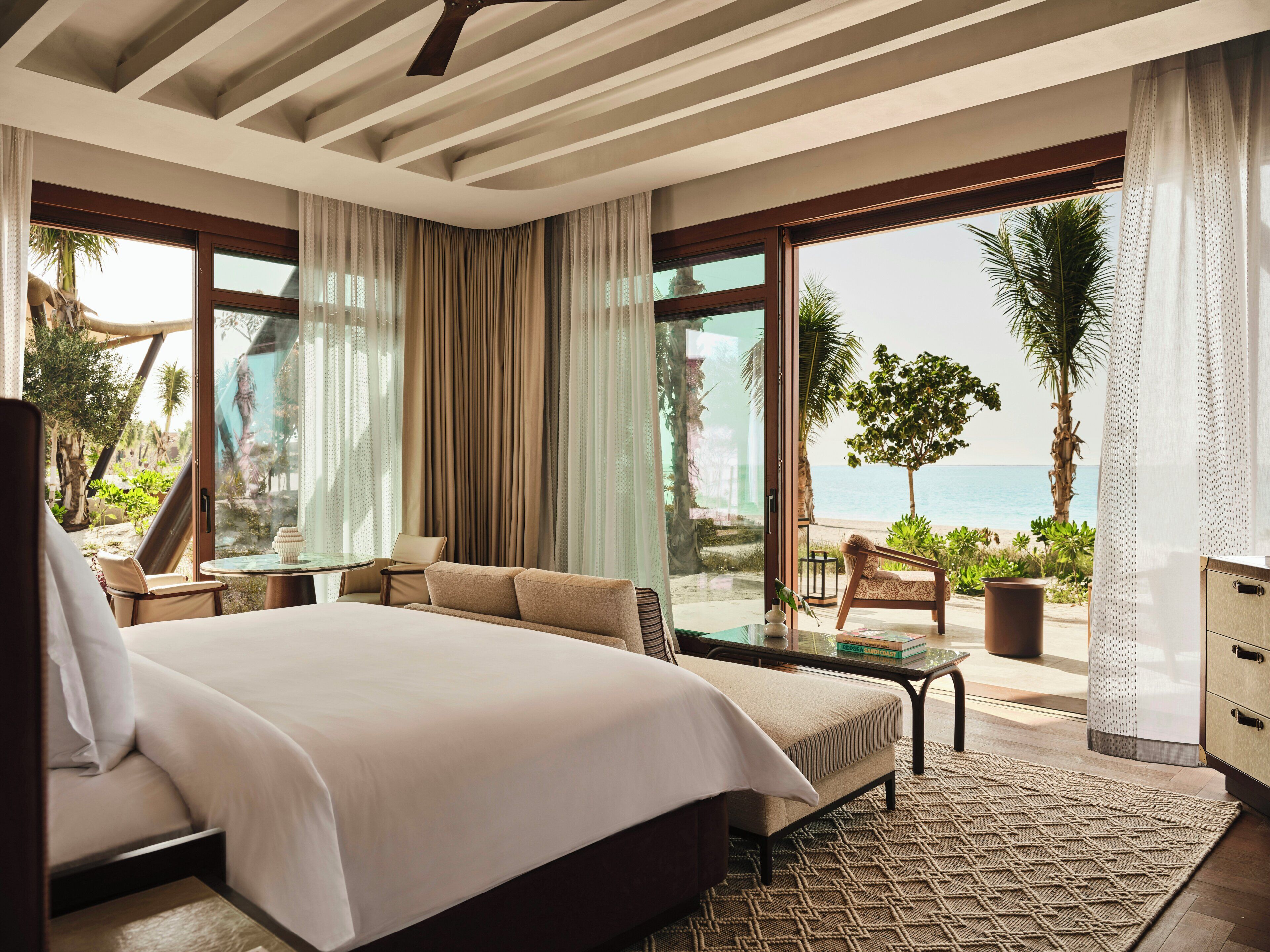 Habitación de hotel con una cama grande, zona de estar con una mesa y vista a la playa.