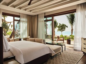 A hotel room with a large bed, a seating area with a table, and a view of the beach.