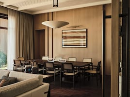 Un comedor con una mesa de madera, sillas, una lámpara colgante y un cuadro abstracto grande en la pared.