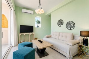 A living room with a sofa, a coffee table, a TV, and a window with a plant.