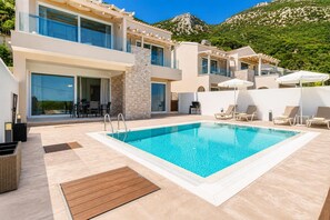 A modern hotel with a swimming pool, outdoor seating, and mountain views.