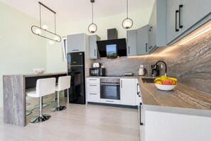 A modern kitchen with a central island, bar stools, a built-in oven, and a large window. - Villa Aglaia - Two Bedroom Villa, Sleeps 4 (Mparmpati)