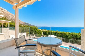 A balcony with a table and chairs, a pool, and a view of the sea and hills. - Villa Aglaia - Two Bedroom Villa, Sleeps 4 (Mparmpati)