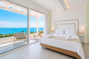 A bedroom with a large bed, a glass door leading to a balcony with a view of the ocean, and two chairs. - Villa Aglaia - Two Bedroom Villa, Sleeps 4 (Mparmpati)