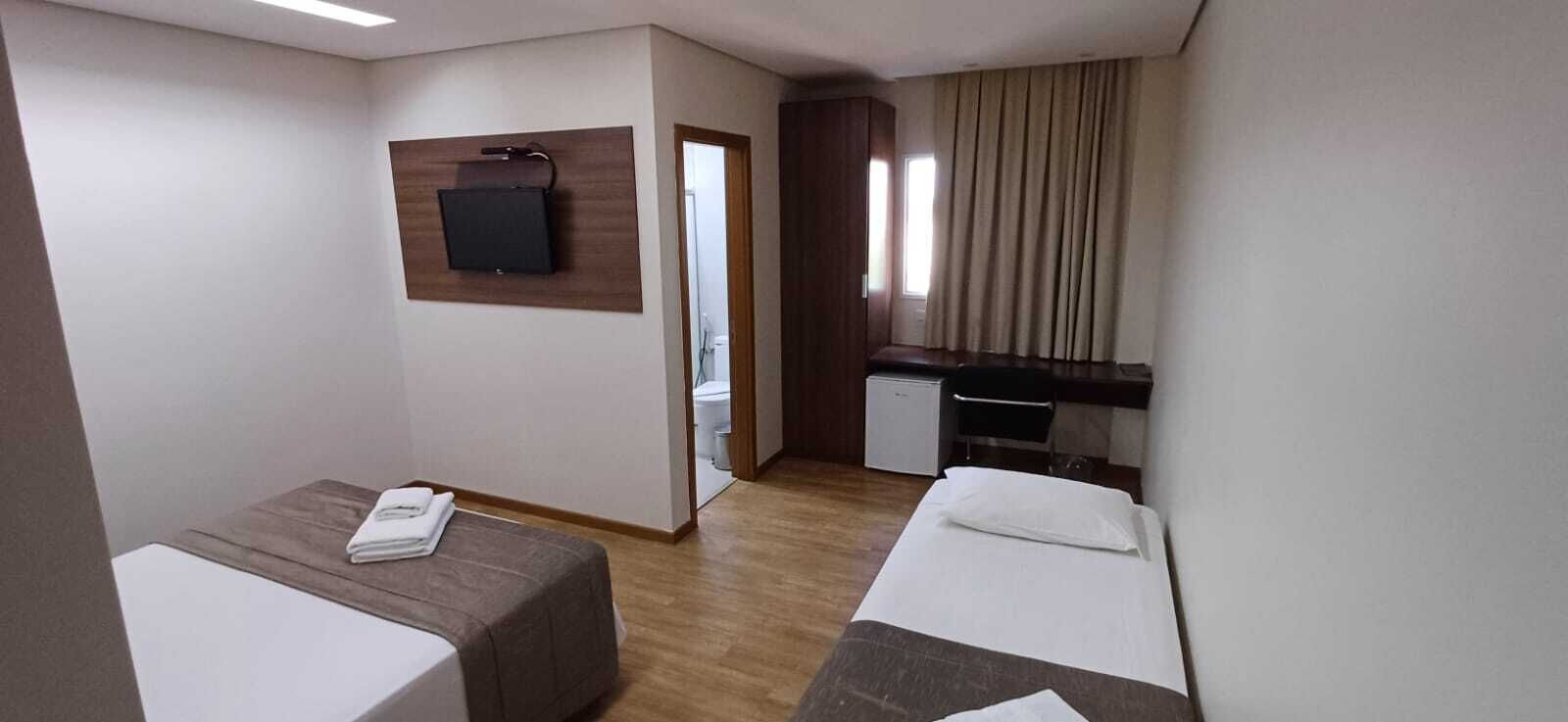 A hotel room with two beds, a desk, a television, and a mirror.