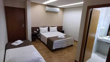 Habitación de hotel con dos camas, una mesita de noche con lámpara, aire acondicionado y baño con lavamanos y espejo.