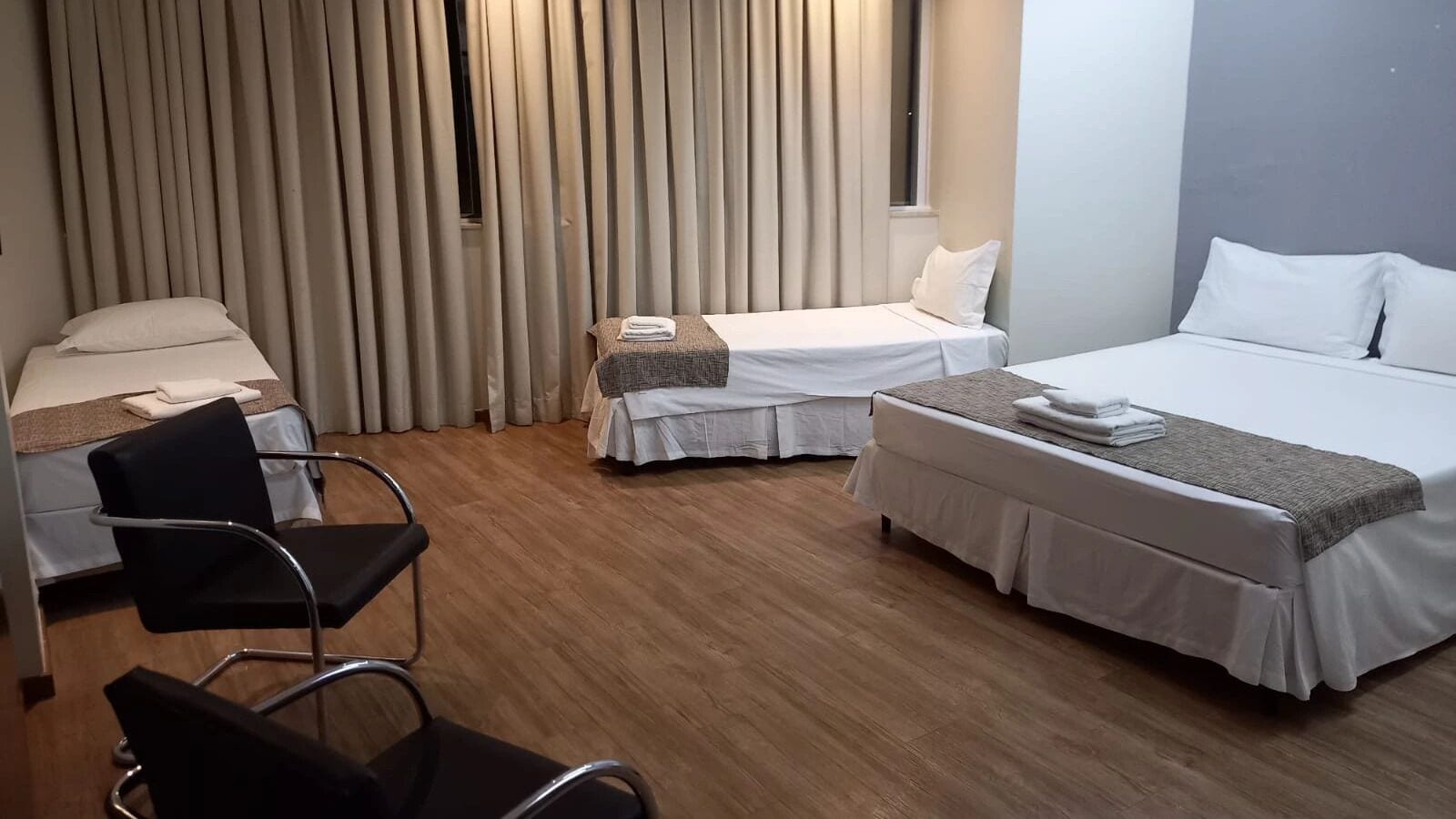 A hotel room with two beds, a chair, and a window with curtains.