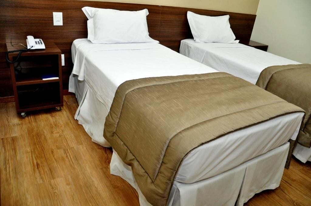 Una camera d'albergo con due letti, un telefono sul comodino e un piccolo ripiano.