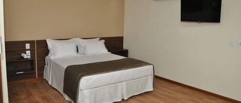 A hotel room with a bed, a nightstand, a TV, and an air conditioning unit.