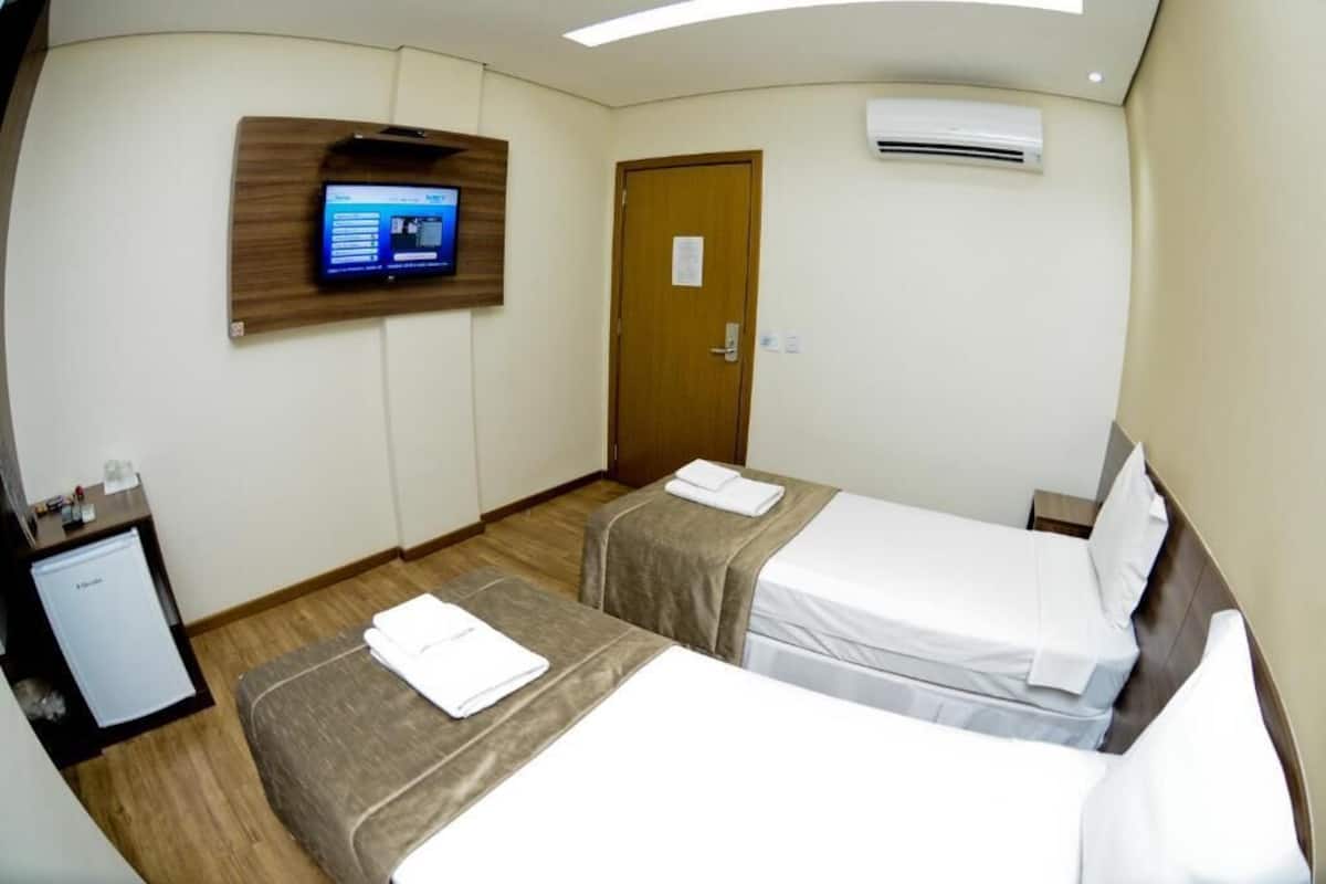 Habitación de hotel con dos camas, un escritorio pequeño con refrigerador, televisor montado en la pared y aire acondicionado.
