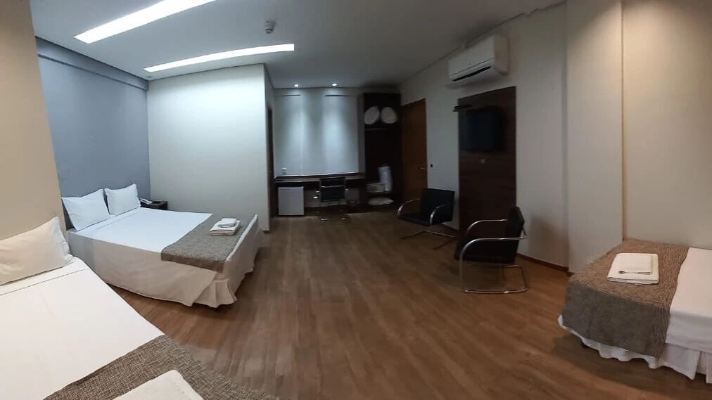 A hotel room with a bed, a desk, a chair, a small kitchenette, and a wardrobe.