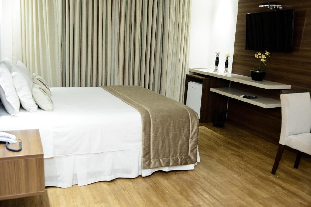 Habitación de hotel con cama, escritorio, silla, televisor montado en la pared y cortina.