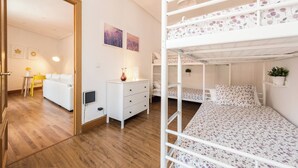 Habitación con literas, un aparador blanco, un sofá blanco y dos lámparas fijadas a la pared.