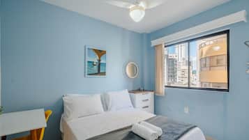 Un dormitorio con cama, escritorio, silla, ventana y vista a la ciudad, además de un ventilador de techo.
