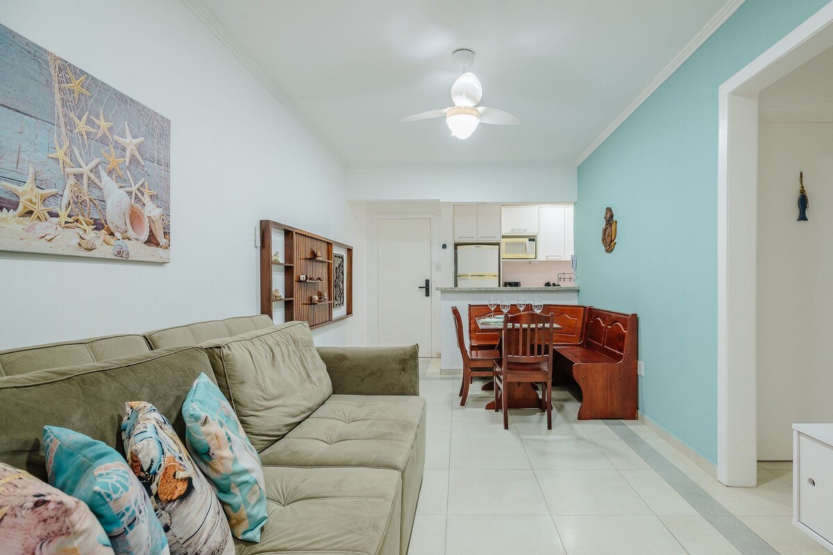 Una sala de estar con sofá, almohadones, una mesa de comedor y sillas. Hay un ventilador de techo y un cuadro en la pared.