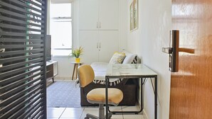 A compact living space with a sofa, a small table, a chair, a potted plant, and a wardrobe. - Apartamento Toscana (Brasília)