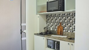 A compact kitchen with a refrigerator, microwave, and a stove. - Apartamento Toscana (Brasília)