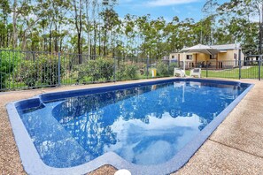A rectangular swimming pool with a clear blue water surface, surrounded by a gravel area and a metal fence. - Vine & Valley Retreat (North Rothbury)