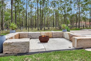 Zona relax esterna con un braciere, circondata da fioriere in pietra e un prato.