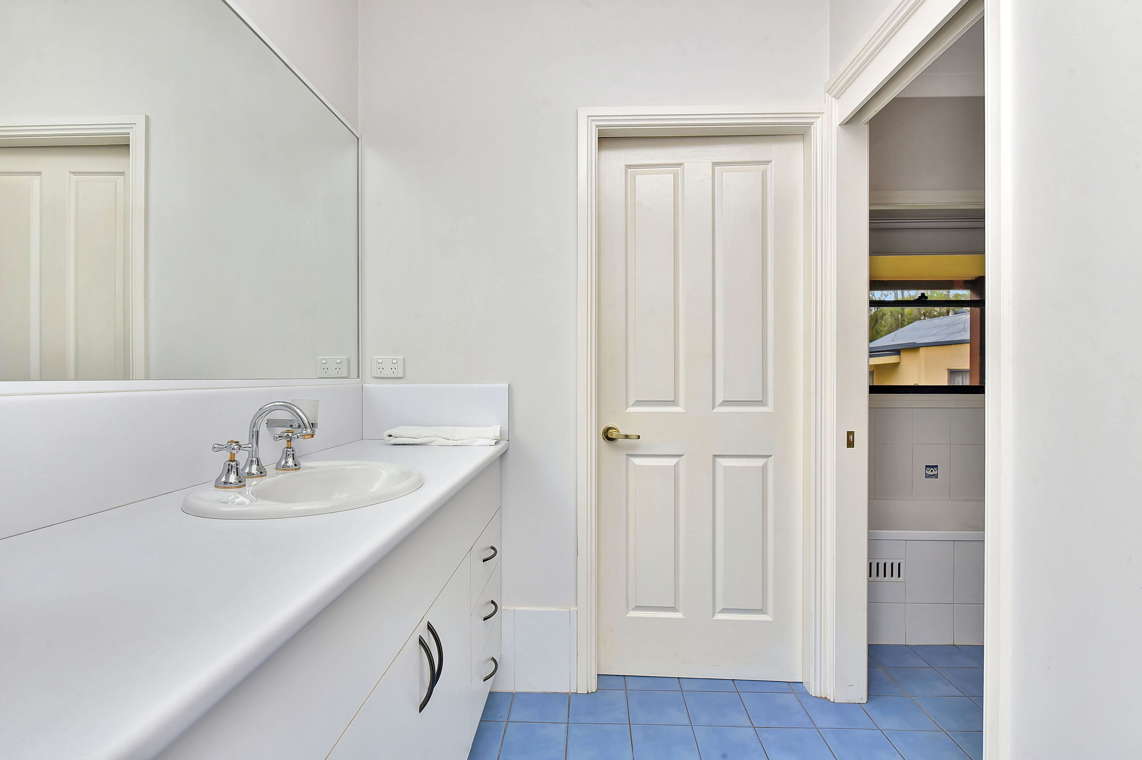 Une salle de bain avec un lavabo blanc, un miroir et une porte donnant sur un couloir.
