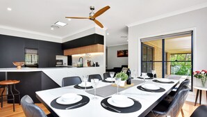Zona pranzo moderna con un tavolo lungo apparecchiato per sei, arredamento bianco e nero e una cucina sullo sfondo.
