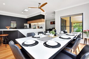 A modern dining area with a long table set for six, black and white decor, and a kitchen in the background. - Vine & Valley Retreat (North Rothbury)