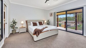 Una camera da letto con un letto, comodini, una ventola a soffitto e vista panoramica attraverso una porta scorrevole in vetro.