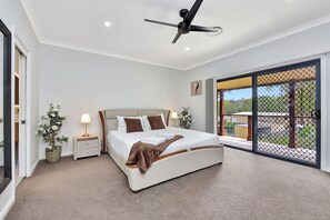 A bedroom with a bed, bedside tables, a ceiling fan, and a view through a sliding glass door. - Vine & Valley Retreat (North Rothbury)