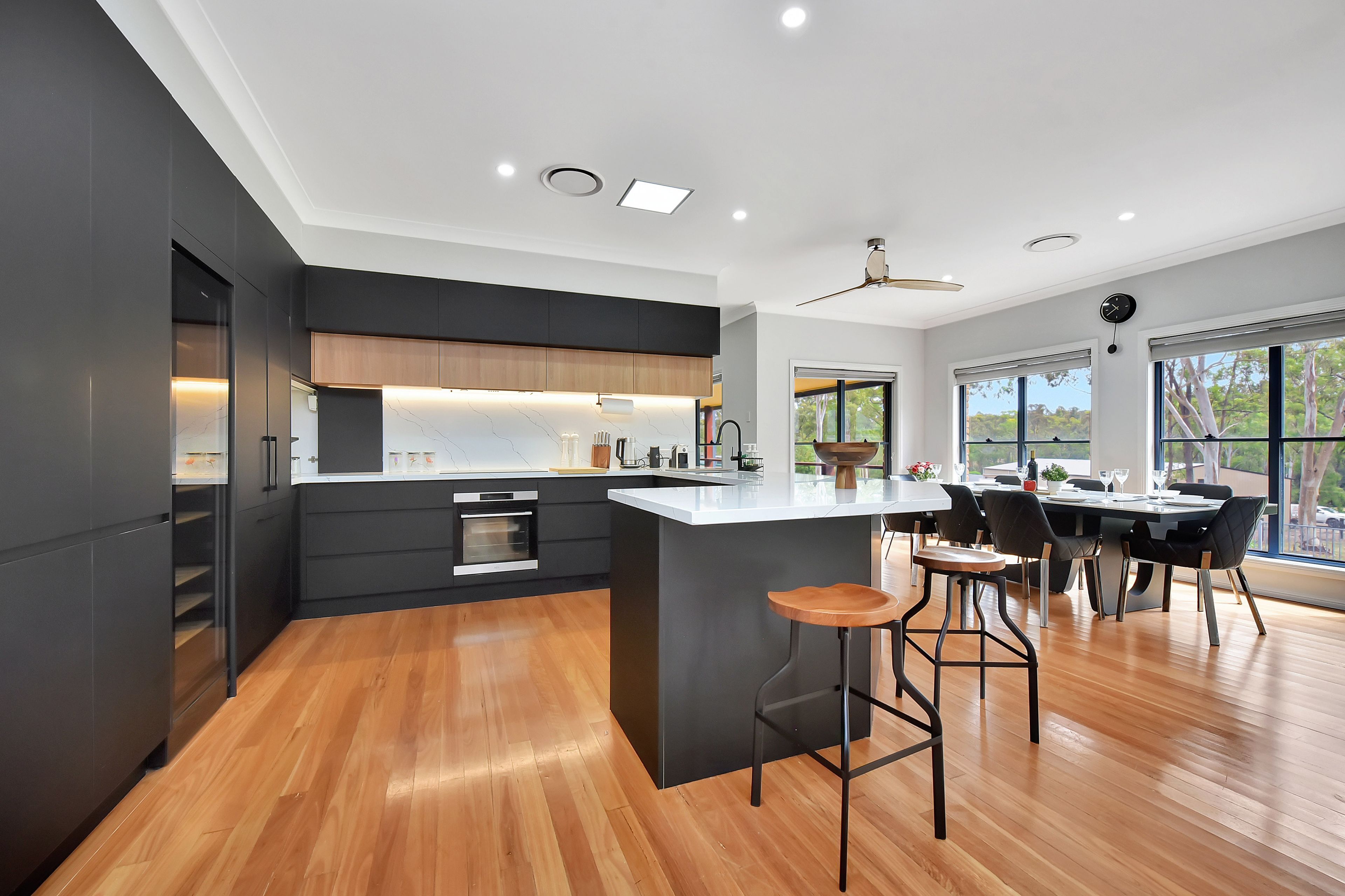 A modern kitchen with a central island, wooden flooring, and a dining area with a view.