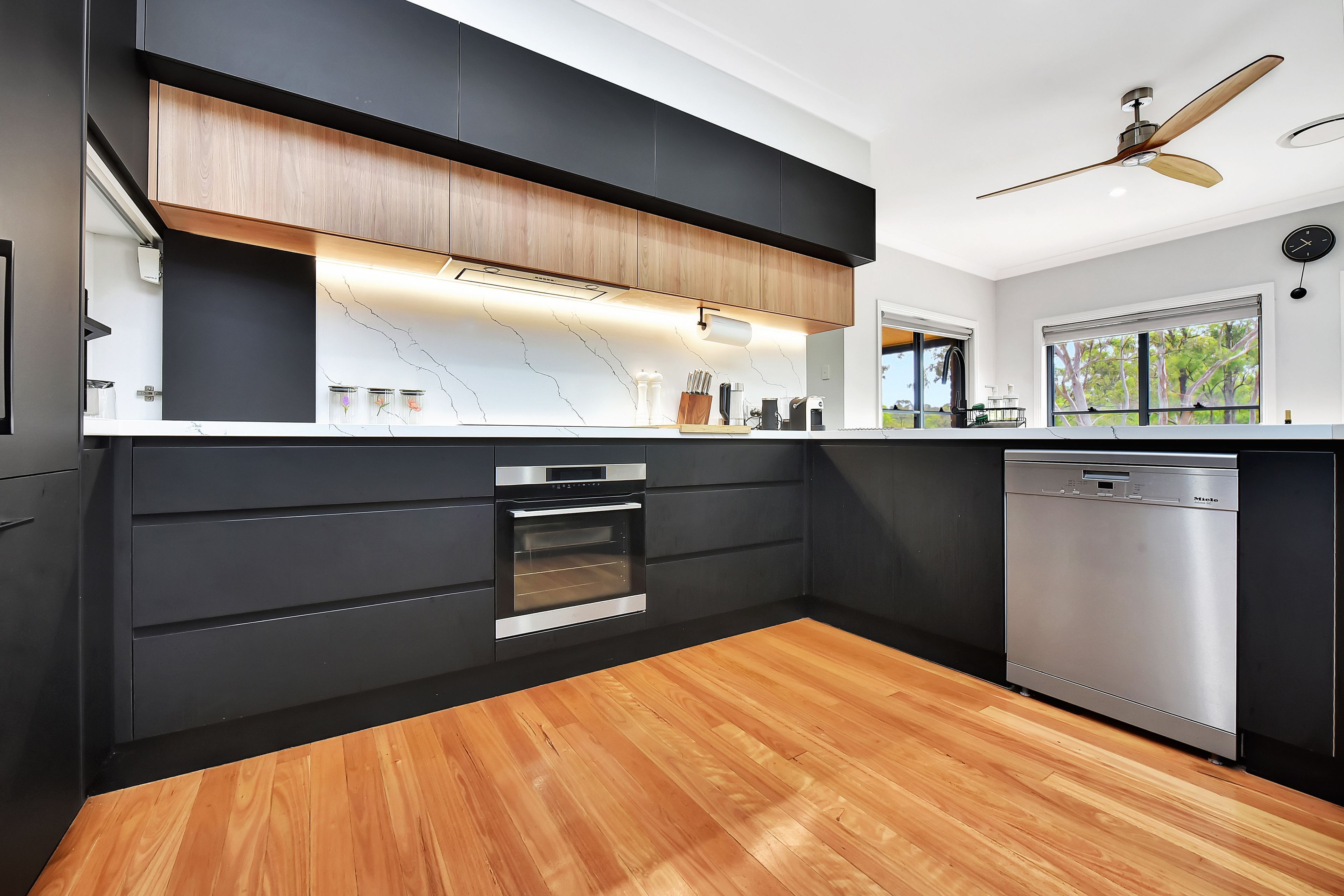 A modern kitchen with a built-in oven, dishwasher, and a wooden floor.