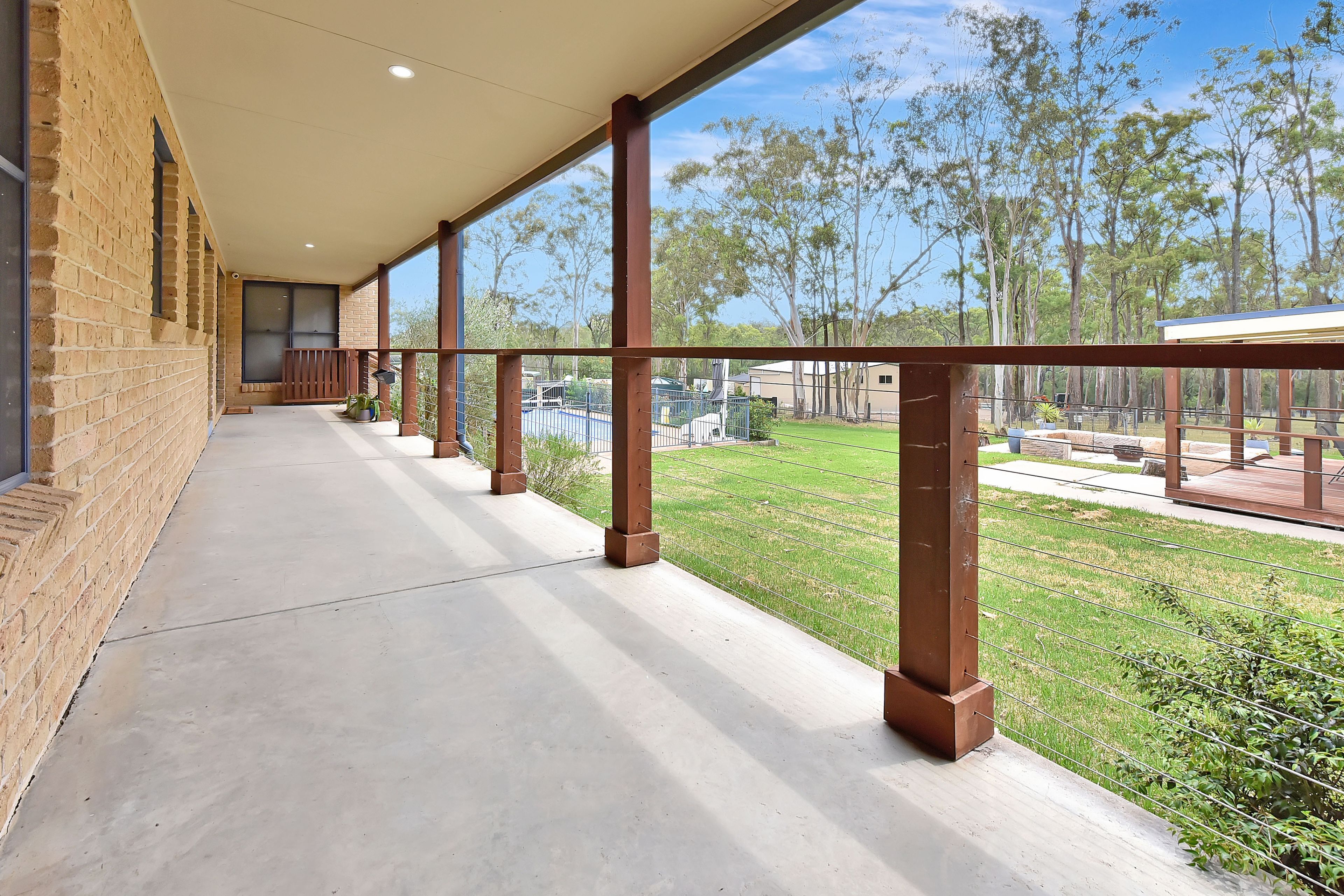 A covered outdoor corridor with a concrete floor, metal railings, and a view of a grassy area with trees.