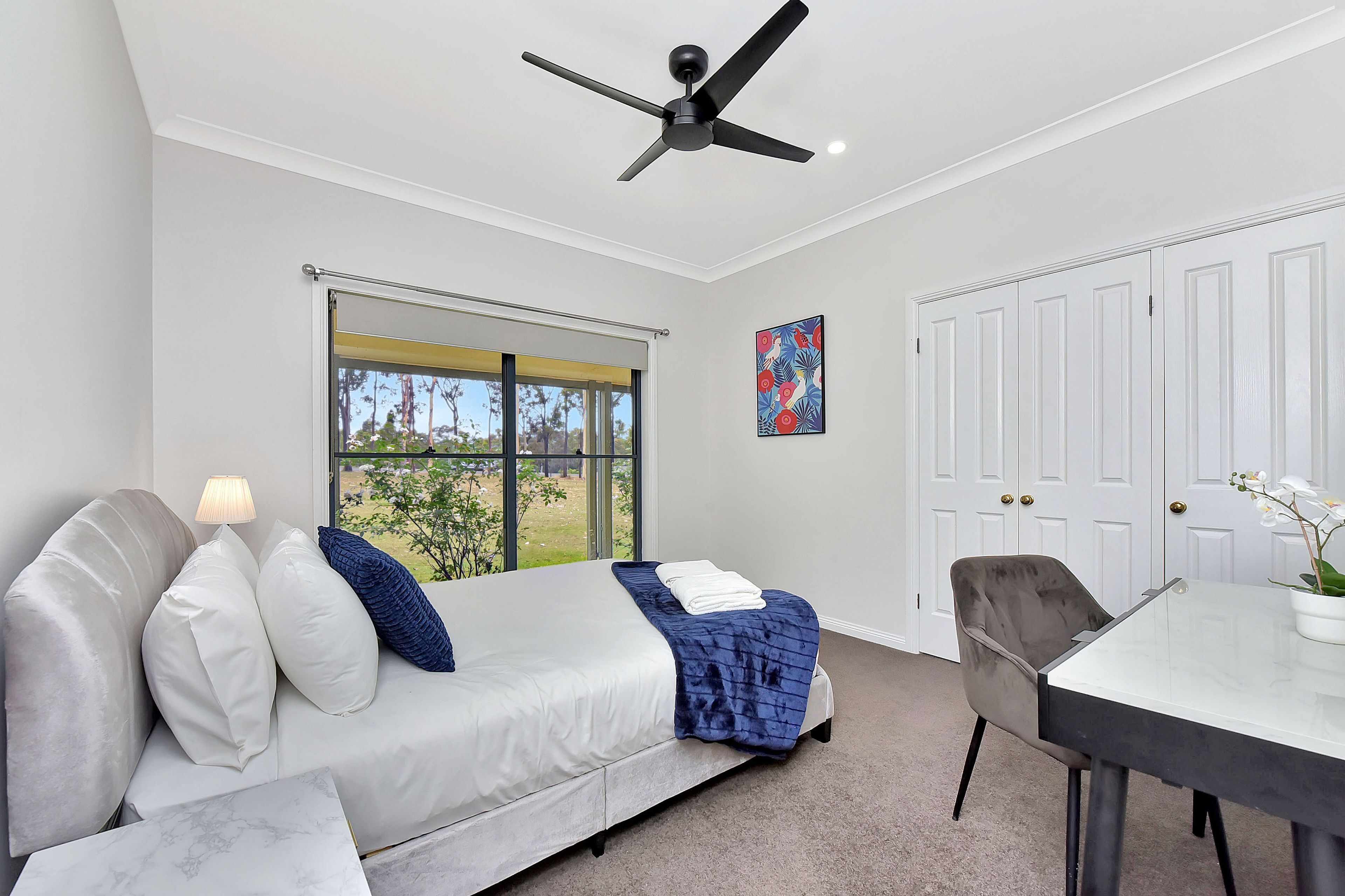 A bedroom with a bed, a window, a ceiling fan, a desk, and a chair.
