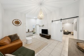 A modern living room with a leather sofa, a television, a chandelier, and a large clock on the wall. - Resort Style Home with Plunge Pool (Cessnock)