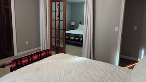 A bedroom with a large bed, a ceiling fan, and a view into another room.