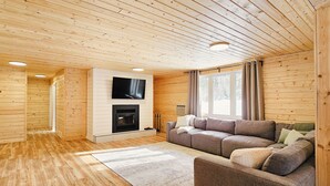 A cozy cabin interior with a wooden ceiling, a fireplace, a sofa, and a TV mounted on the wall. - Faloma Lakeside Cabins (Faloma)