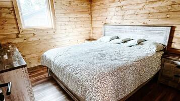 A wooden cabin bedroom with a bed, a nightstand, a window, and a wooden floor.