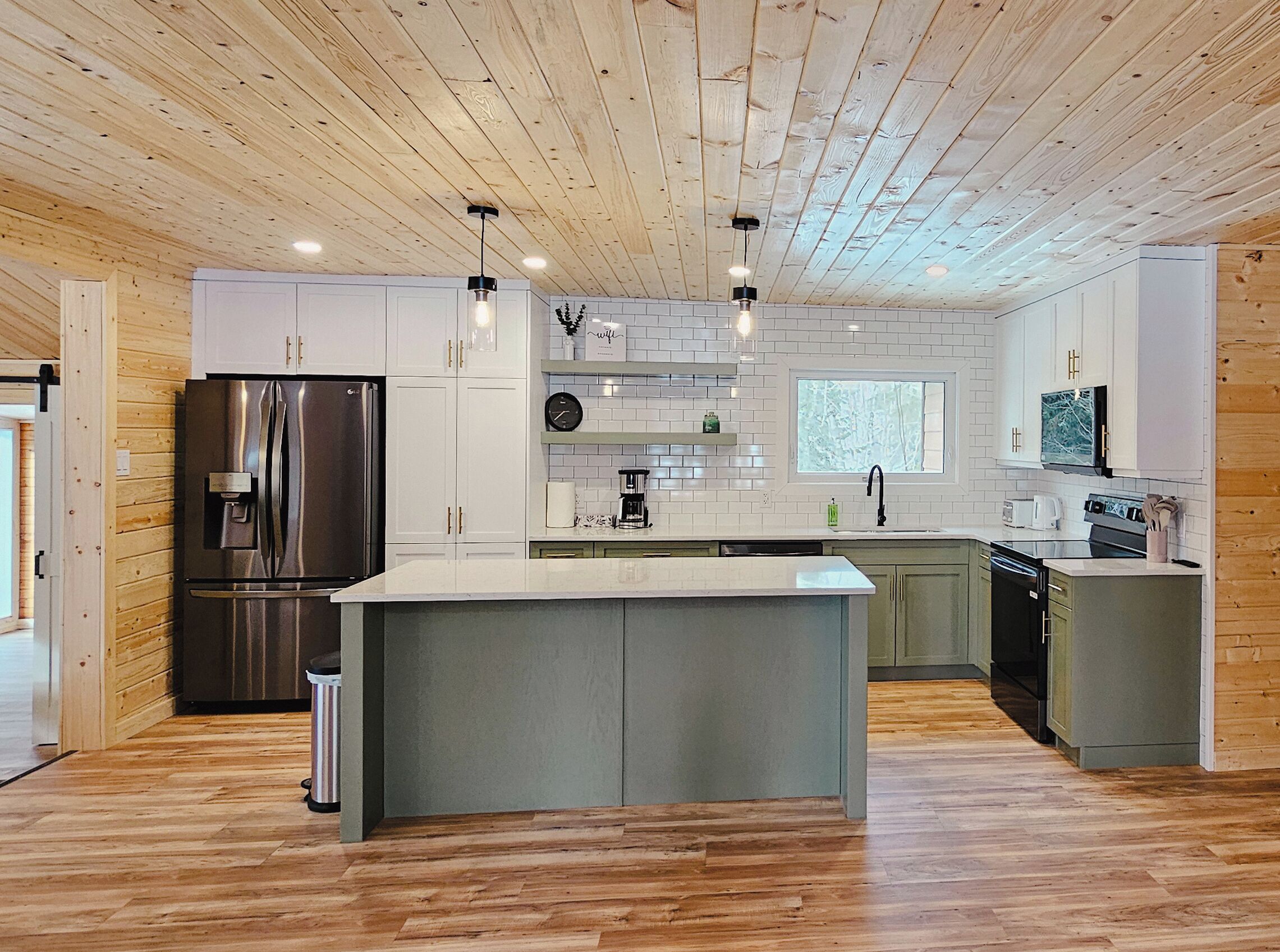 Una cocina moderna con techo de madera, armarios blancos, una isla central y electrodomésticos de acero inoxidable.