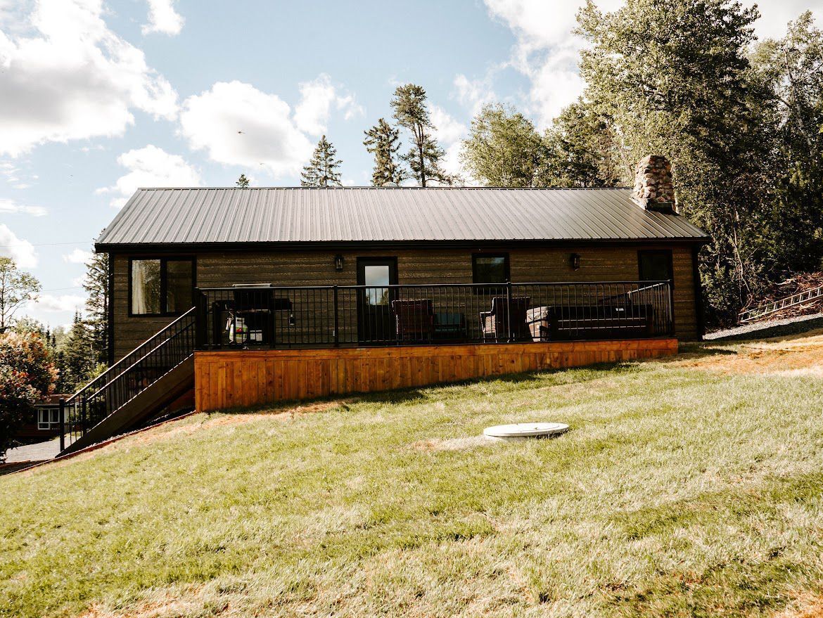 A modern cabin with a metal roof, wooden deck, and a staircase leading to the entrance.