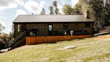 A modern cabin with a metal roof, wooden deck, and a staircase leading to the entrance.