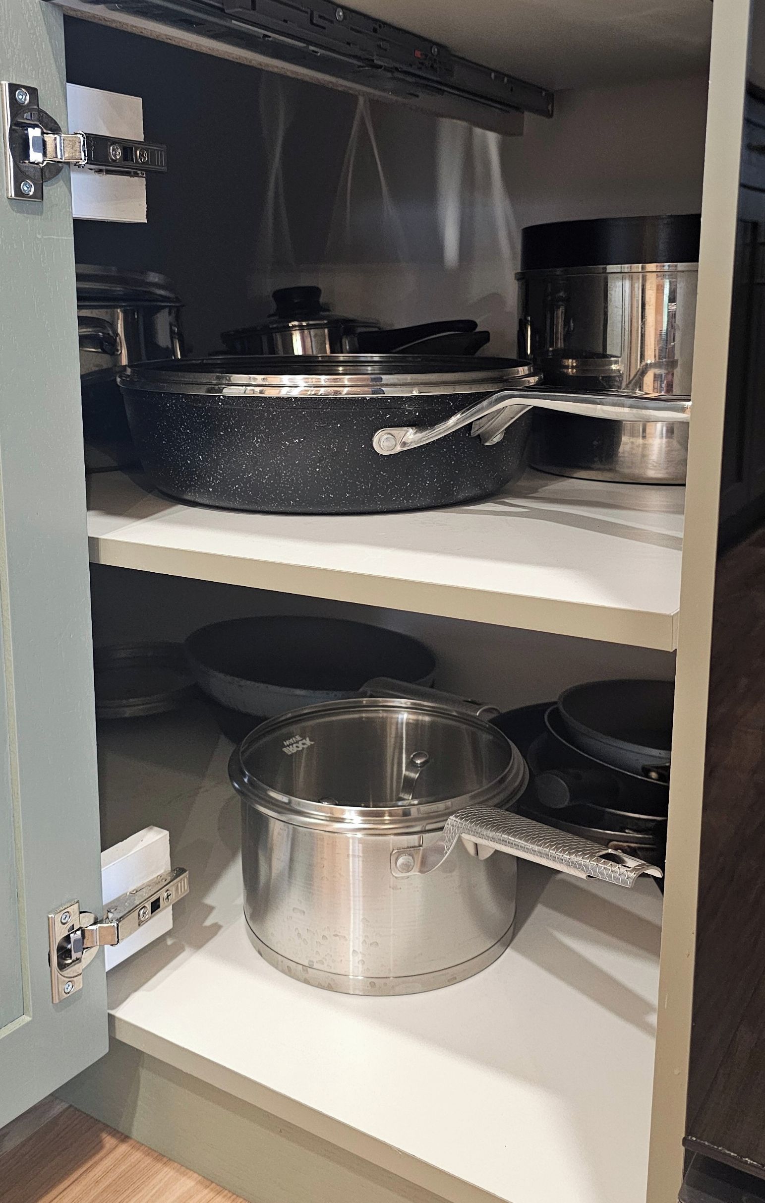 Een keuken met roestvrijstalen kookgerei op planken, waaronder een koekenpan en pannen.