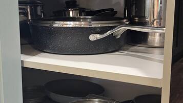 Een keuken met roestvrijstalen kookgerei op planken, waaronder een koekenpan en pannen.