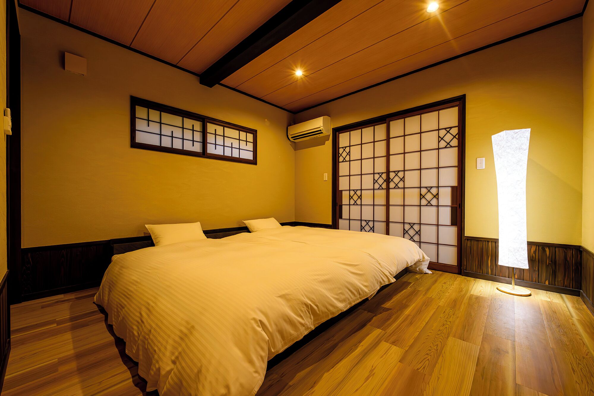 A room with a large bed, wooden flooring, a traditional sliding door, and a ceiling light.