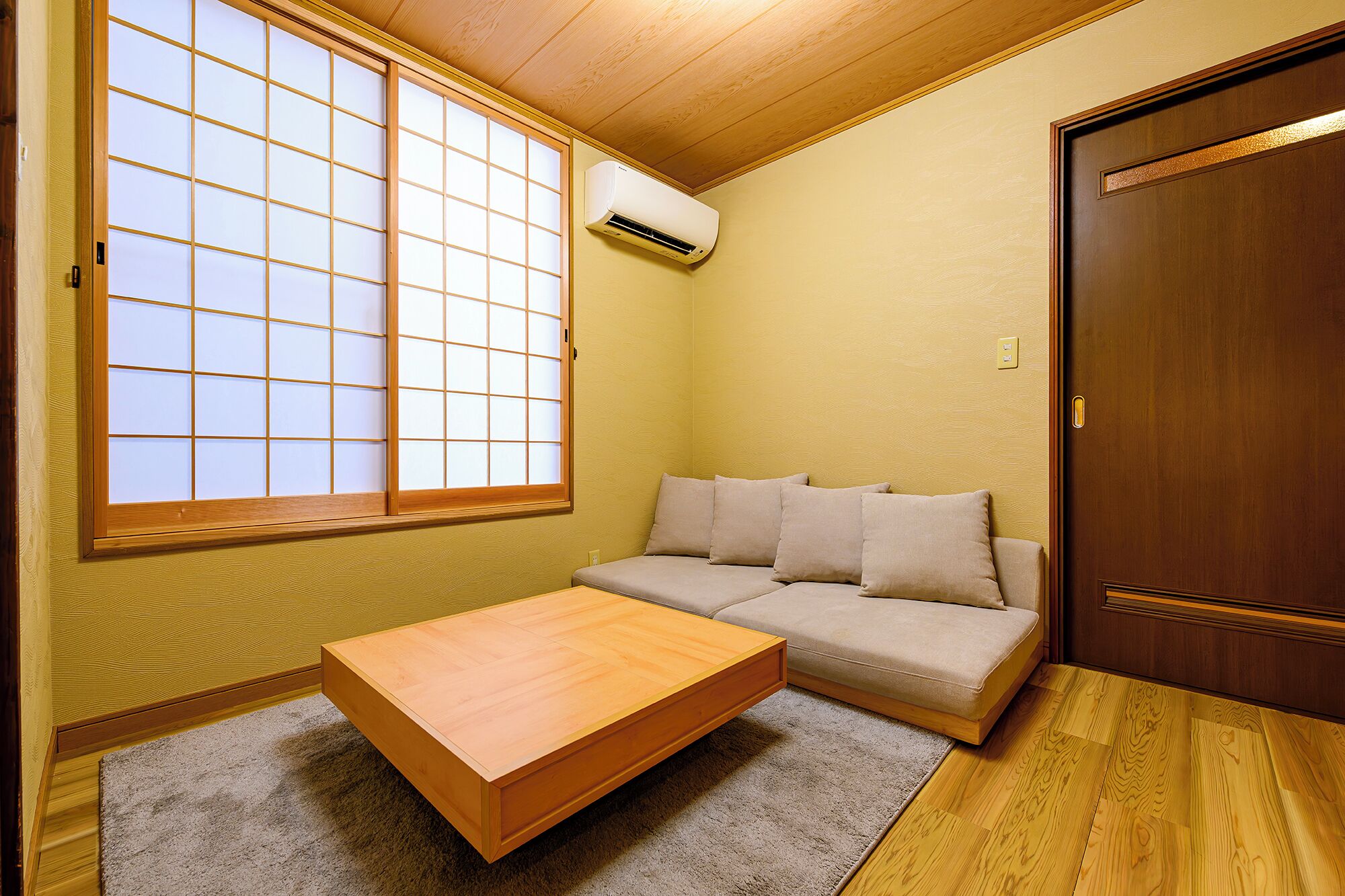A room with a sliding shoji screen window, a sofa, a wooden table, and a door.