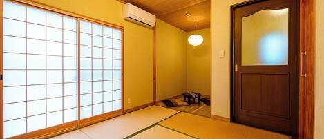 A traditional Japanese room with tatami flooring, a sliding shoji door, a wooden ceiling, and a dark wooden door with a frosted glass panel.